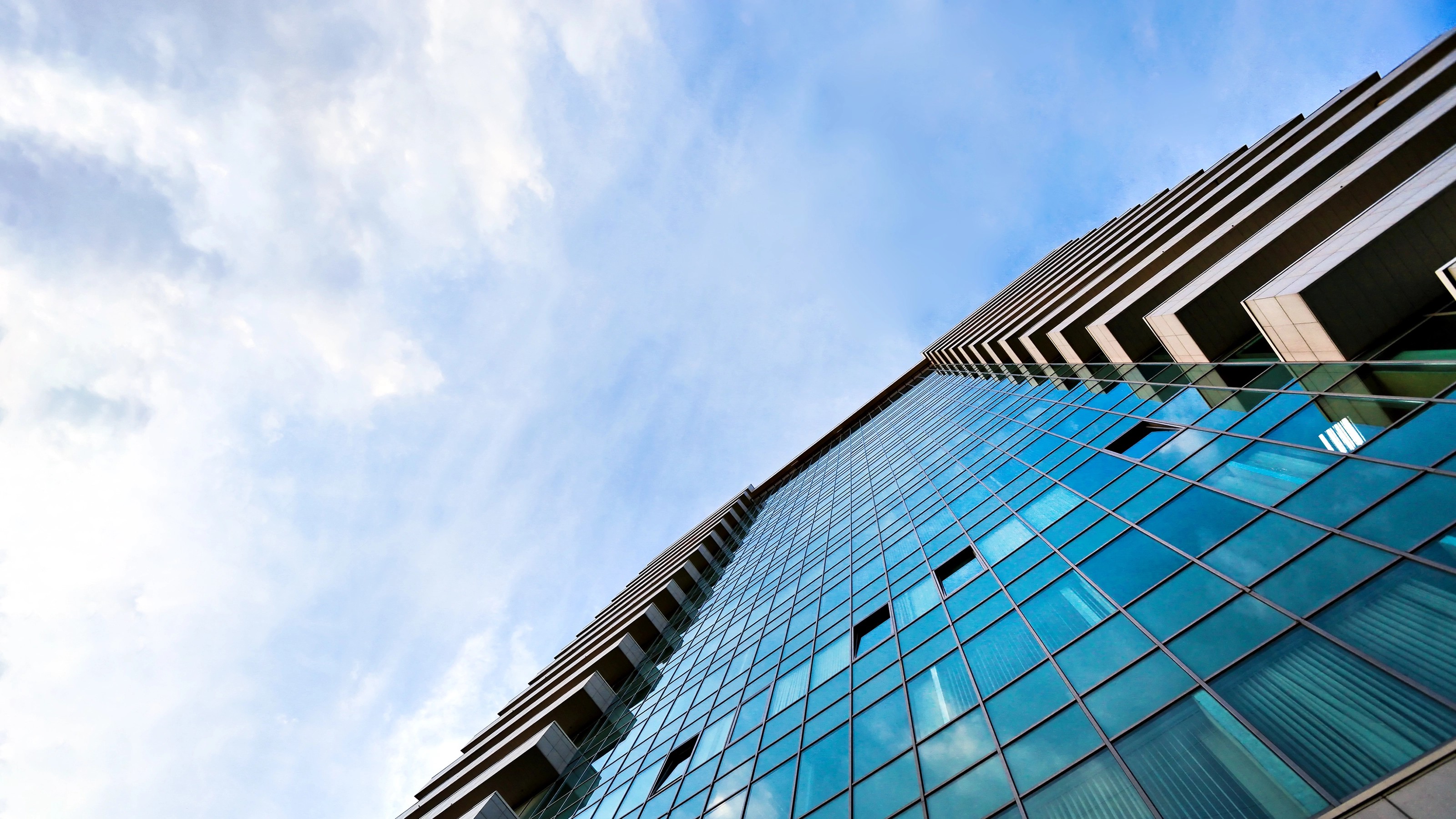 Low-angle view of a modern glass building reflecting blue sky and clouds.